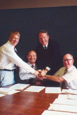 Cuatro hombres blancos con papeles de trabajo se dan la mano en grupo